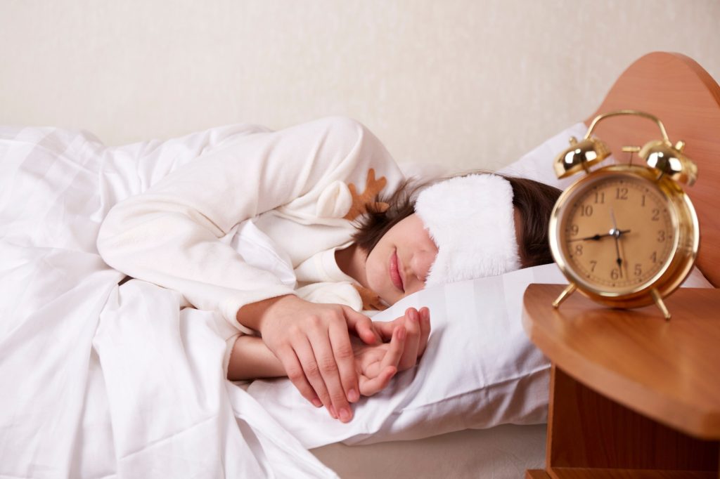 A young girl sleeps in bed wearing a sleep mask.