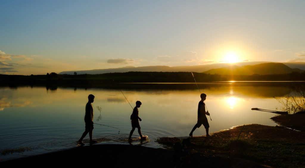 Silhouettes of fishing boys are walking home after fishing the lake in the evening sun